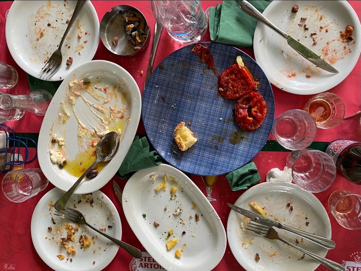 Overhead view of a red table covered in empty plates, glasses and cutlery after a long meal at home